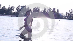 Sexy blonde girl in bikini enters a lake at sunset