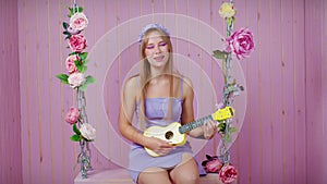 Sexy blonde girl sit on swing with ukulele, sings