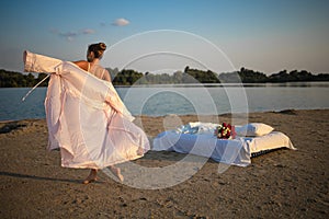 Sexy Blonde Woman in lingerie Holds Flower bouquet On Beach At Sunset.