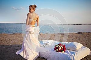 Sexy Blonde Woman in lingerie Holds Flower bouquet On Beach At Sunset.