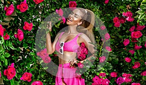 Sexy blonde woman in pink bikini on the sun-tanned slim and shapely body is posing in  roses garden - Image. Bikini fashion.