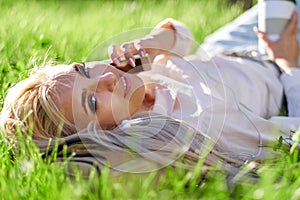 Sexy blonde woman talking on the mobile phone and lying on meadow