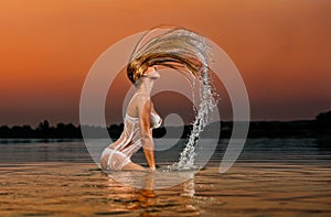 Blondínka žena vo vode na západ slnka 