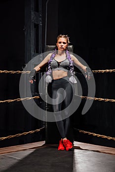 boxing girl stands leaned on ropes of competition ring.