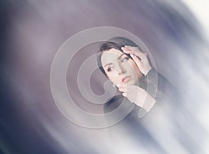 Sexy brunette in black on a black background gracefully touches her face with her fingers.