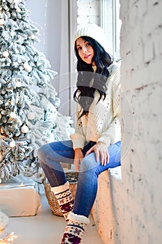 Sexy brunette girl in sweater and jeans in front of her Christmas tree