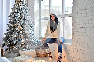 Sexy brunette girl in sweater and jeans in front of her Christmas tree