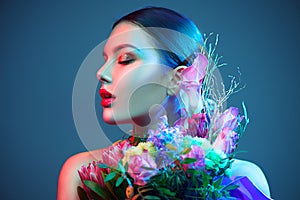 Sexy brunette model girl with bouquet of beautiful flowers. Beauty young woman with bunch of flowers in colorful neon lights photo