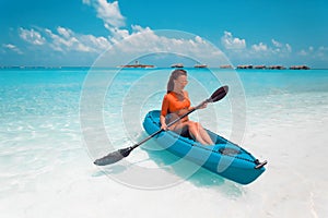 Sexy brunette paddling a kayak. Woman exploring calm tropical bay. Maldives. Sport, recreation. Summer water sport, adventure