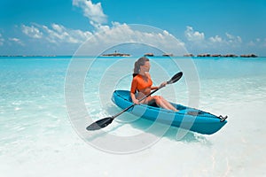 Sexy brunette paddling a kayak. Woman exploring calm tropical bay. Maldives. Sport, recreation. Summer water sport, adventure