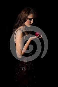 brunette woman with dark red dress looking down at red apple in her hand