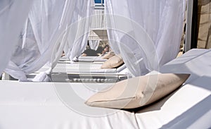 Sexy, brunette woman lying behind many white curtains in a black bathrobe on cot bed in the sunny hotel wellness spa resort in