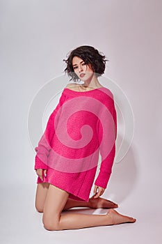 Sexy brunette woman with short hair in a pink sweater poses on a white background. Classic bright makeup on a woman face