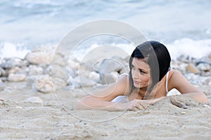 brunette woman, wear wet t-shirt as she lie on sandy beach