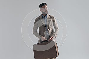 Sexy businessman with beard holding suitcase and looking to side