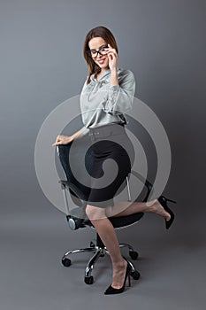 Sexy businesswoman posing on chair and adjusting eyeglasses