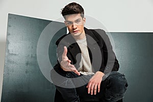 sexy casual man in black coat crouching, looking forward and shaking hand