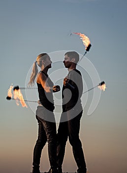 Sexy couple of fire dancers spin flaming poi on idyllic evening blue sky outdoors, motion