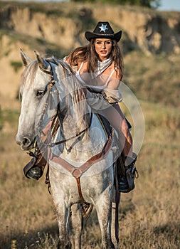 Sexy cowgirl with hat on horseback in the desert. Beautiful girl in a cowboy hat on a horse.