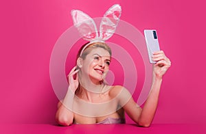 Sexy easter bunny woman with rabbit ears having call holding smart phone in hand shooting selfie on front camera