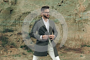 Sexy elegant man with glasses buttoning long coat and looking to side