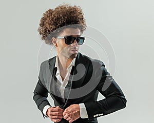 sexy elegant man with sunglasses looking to side and buttoning tuxedo