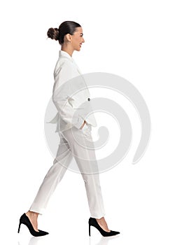 sexy elegant woman in white suit with bun hair walking with hands in pockets