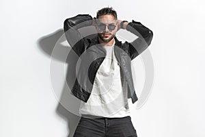 Sexy fashion man in leather jacket holding hands behind head and posing