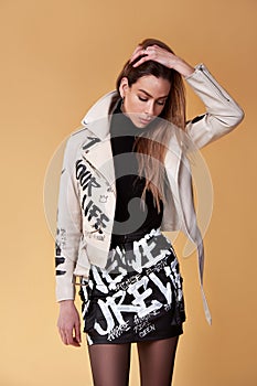 Sexy fashion model brunette hair wear trendy clothes leather jacket beige and black short skirt painting lettering word style