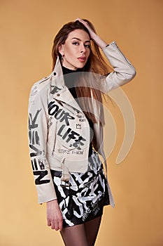 Sexy fashion model brunette hair wear trendy clothes leather jacket beige and black short skirt painting lettering word style