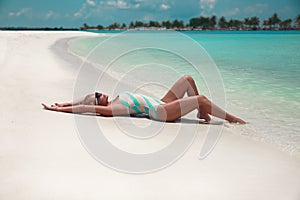 Sexy fashion woman chilling on white sand. Slim blonde in bright swimwear resting on tropical beach. Summer vacations, idyllic