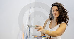 Sexy female beauty artist portrait of curly hair woman in casual white underskirt with brush and palette painting on the studio