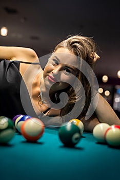 Sexy female pool player wear black dress lying on billiard table