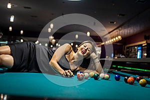 Sexy female pool player wear black dress lying on billiard table