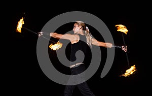 Sexy fire dancer manipulate burning batons during night performance in dark outdoors, party