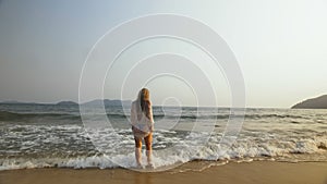 Woman in a white tunic on the beach, near the stormy sea. Blonde