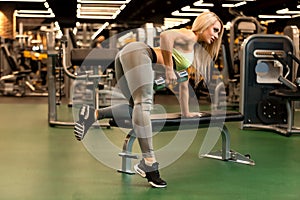 Sexy fitness blonde woman is doing one-arm dumbbell row on the bench