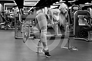 Sexy fitness blonde woman is doing one-arm dumbbell row on the bench BW