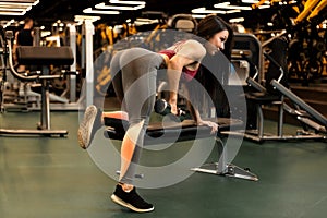 Sexy fitness brunette girl is doing one-arm dumbbell row on the bench