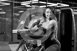 Sexy fitness brunette girl is sitting and doing biceps curls on trainer BW