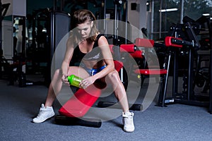 fitness woman in sportswear resting after dumbbells exercises in gym. Beautiful girl with perfect fitness body drinking from