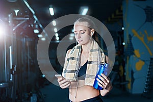 fitness woman in sportswear resting after dumbbells exercises in gym. Beautiful girl with shaker and towel.