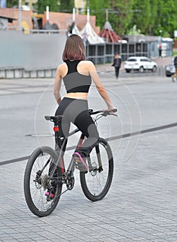 Sexy fitness. Young beautiful woman in black sport wear posing outdoor on the bicycle at the stadium