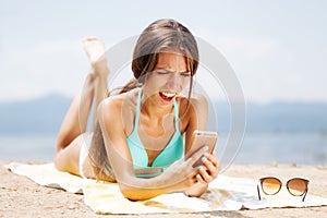 Surprised girl with phone on a beach