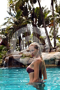 girl with blond hair in bikini relaxing in outdoor swimming pool