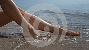 Sexy girl feet washed by sea waves close up. Barefoot woman sinking legs in sand