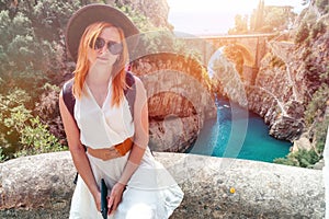 A sexy girl in a hat with a backpack enjoys an incredibly beautiful view of a stone bridge over the gorge Fiordo di Furore. Little photo
