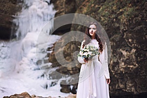 A girl is holding a wedding bouquet of flowers against the background of a glacier and mountains