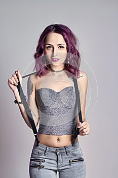 girl with purple hair and a tattoo on the body posing on grey background. Perfect woman in gray jeans and a t-shirt, bright