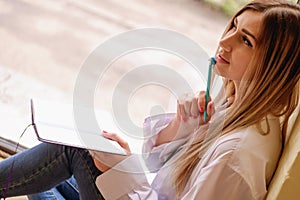 Sexy girl sitting at the table with notebook and pen. single woman in white men`s shirt thinking about something, working.